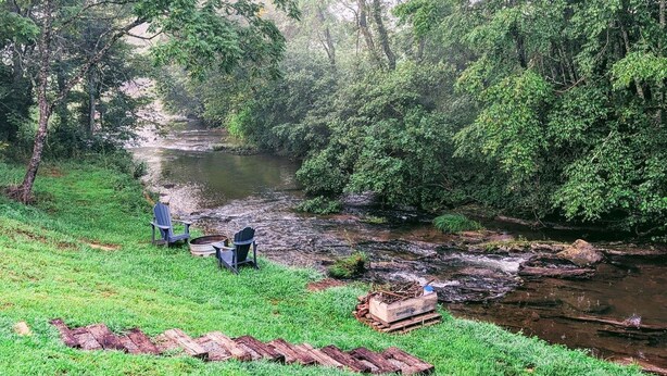 Un entorno junto al río con zona verde, una banca y una pequeña estructura de madera.