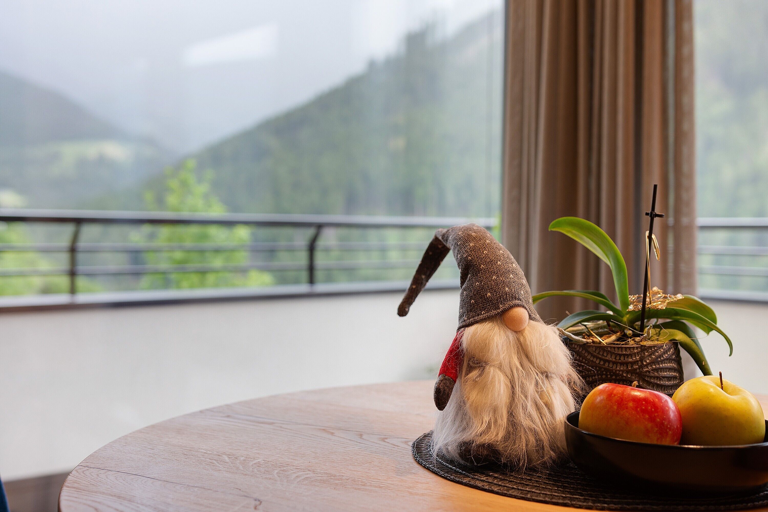 Une poupée est posée sur une table, à côté d’un bol de pommes et d’une plante en pot.