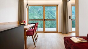 A modern room with a dining area, a red sofa, and a large window with a view of a forested mountain. - Apartment 'Similde' with Mountain View, Shared Terrace and Wi-Fi (Tiers)