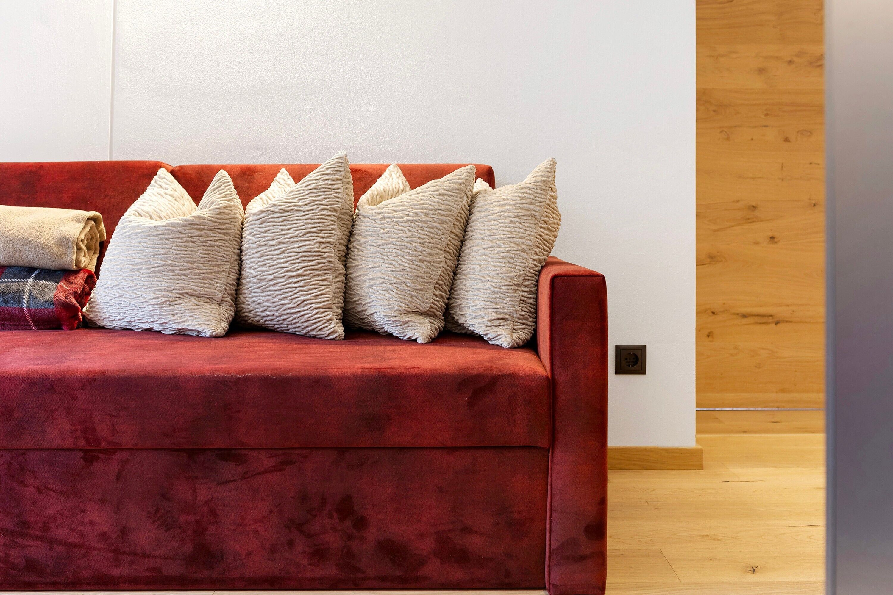 Ein rotes Sofa mit strukturierten Kissen vor einer weißen Wand und Holzboden.