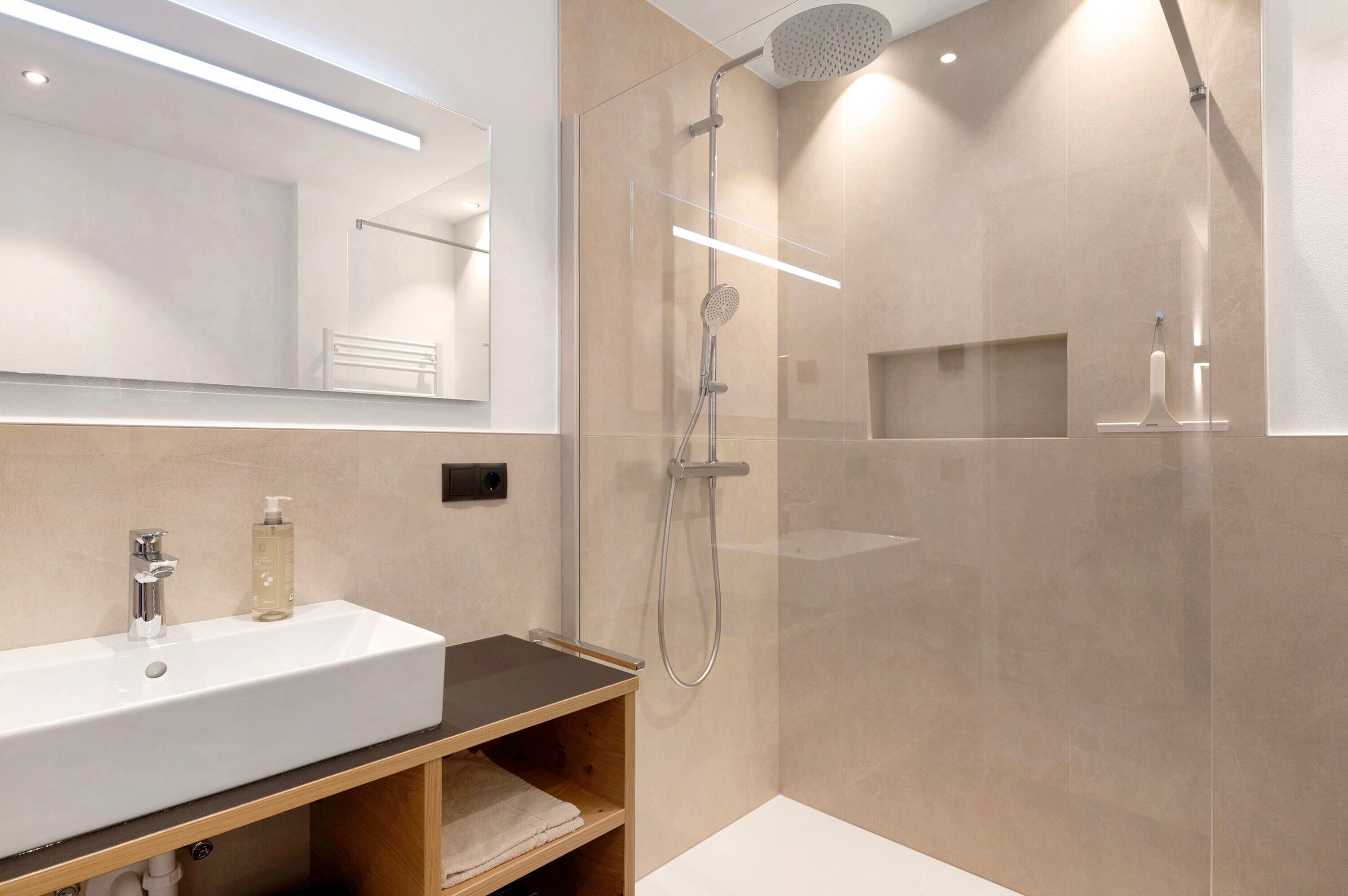A modern bathroom with a large mirror, a sink, a shower, and a vanity with a towel rack.