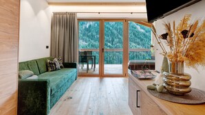 Ein modernes Interieur mit einem grünen Sofa, Holzböden, einem Essbereich und Blick auf eine bewaldete Landschaft durch große Glasüren.