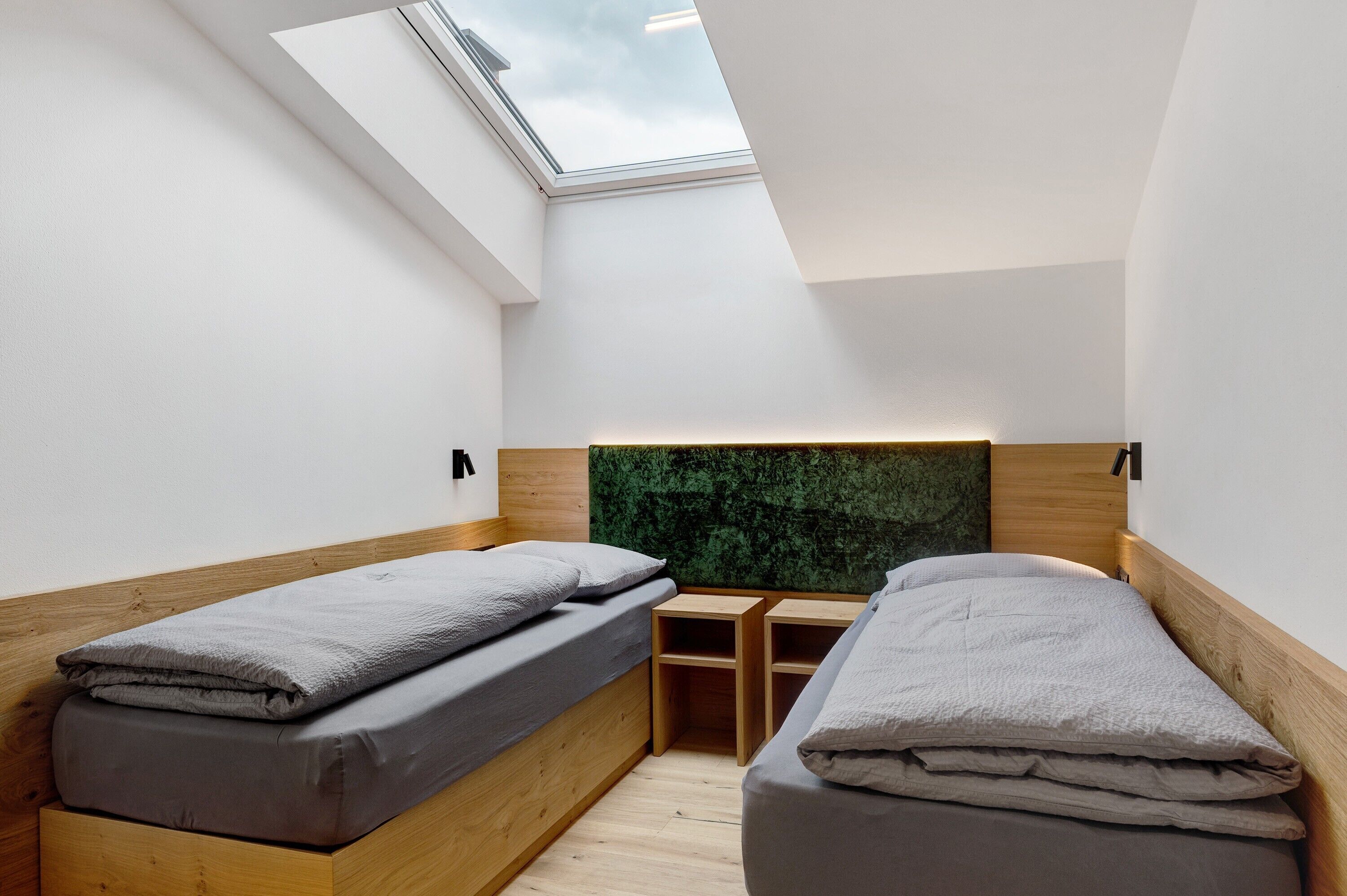 A small, modern bedroom with two single beds, a skylight, and a green wall feature.