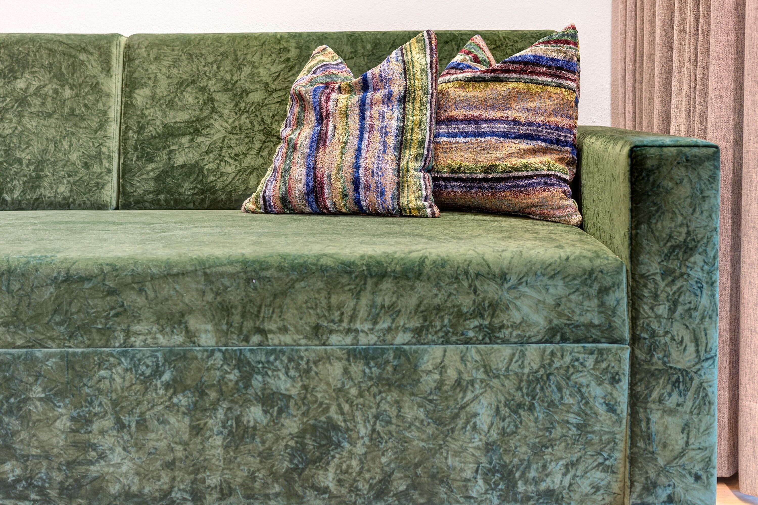A green upholstered sofa with striped pillows.
