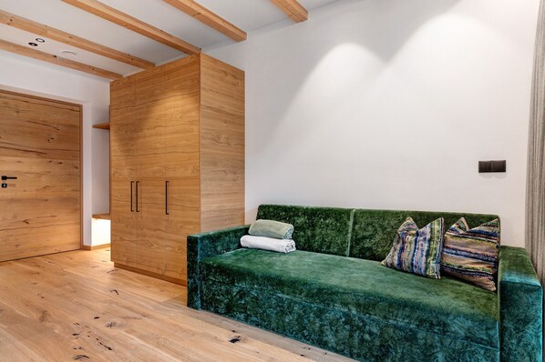 A room with a green velvet sofa, wooden wardrobe, and a wooden floor.