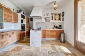 A kitchen with wooden cabinets, a marble island, a coffee maker, and a trash can.