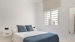 Ein Schlafzimmer mit einem Bett, Nachttischen, einem Fenster und einem an der Wand befestigten Spiegel.