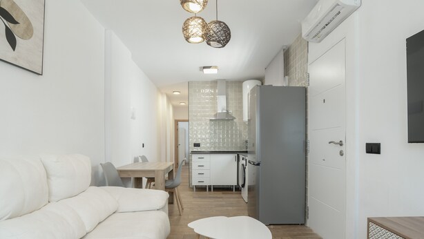 Eine moderne Küche mit weißen Schränken, einem grauen Kühlschrank und einem Essbereich mit weißem Tisch und Stühlen.