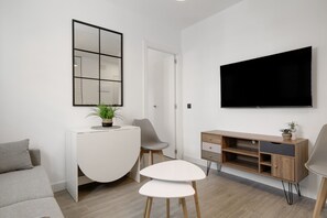Een moderne woonkamer met een flatscreen televisie, een witte console tafel met een plant, een grijze bank en een kleine witte tafel.