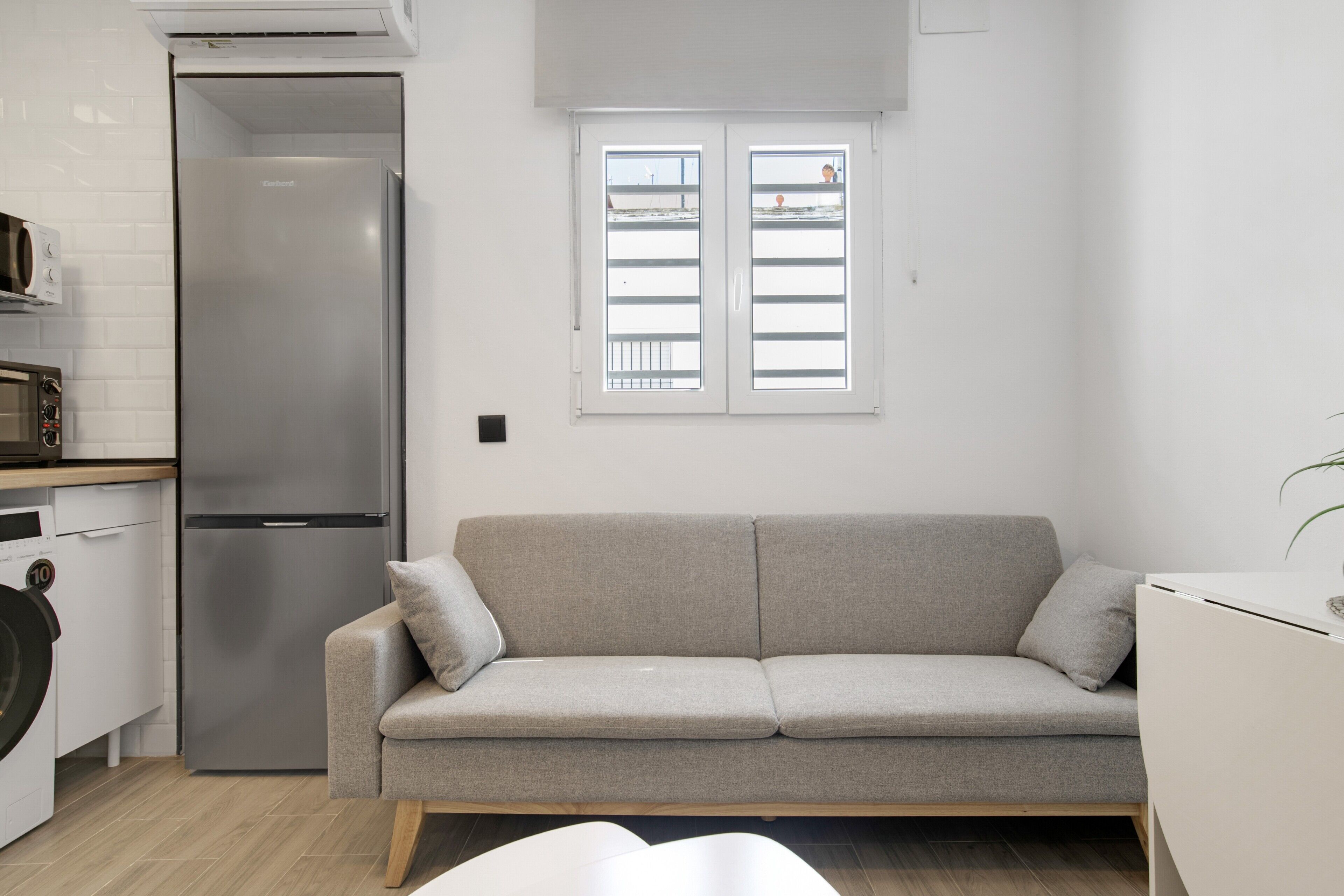 A compact kitchen with a built-in refrigerator, a washing machine, and a window with blinds.