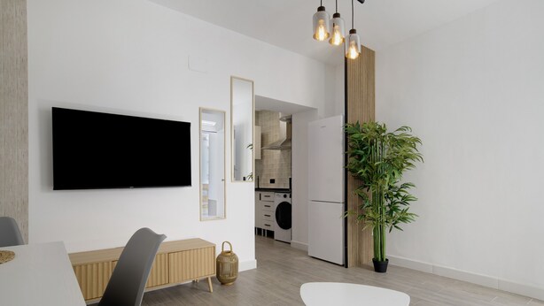 A modern kitchen with a flat-screen TV, wooden cabinets, and a dining area with a white table and chairs. - Apartment 'Apartamentos Habana 4' with Air Conditioning (Barbate)