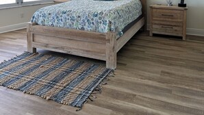 Une chambre avec un lit en bois, un ventilateur de plafond, une vue sur l’océan, deux tableaux encadrés représentant des tortues de mer et une table de chevet avec une lampe.