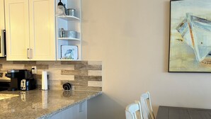 Une cuisine avec des meubles blancs, un plan de travail en granit et un coin repas comprenant une table en bois et deux chaises.