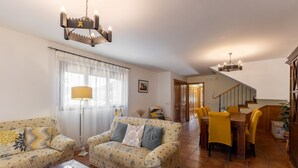Un soggiorno con divano, tavolino, tavolo da pranzo con sedie, una scala e un lampadario.