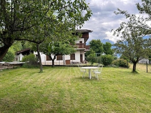 Un bâtiment à deux étages doté d’un balcon, entouré d’une pelouse verdoyante et d’arbres.