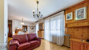 A living room with a red leather sofa, wooden cabinets, a chandelier, and a dining area in the background. - Apartment 'Primo Piano 2' with Mountain View, Private Terrace and Wi-Fi (Pieve di Cadore)