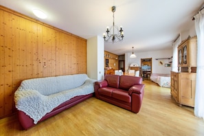Un salon chaleureux avec un canapé rouge, un divan recouvert de tissu blanc, des boiseries, un lustre et un meuble en bois.