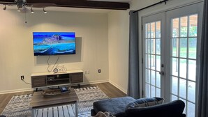 Ein Wohnzimmer mit an der Wand montiertem Fernseher, Holzboden, einer Schiebeglastür und einem gemusterten Teppich.