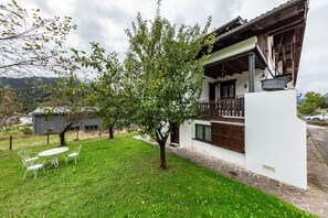 Ein weißes Gebäude mit einem Balkon, ein Baum im Hof und ein Tisch mit Stühlen.