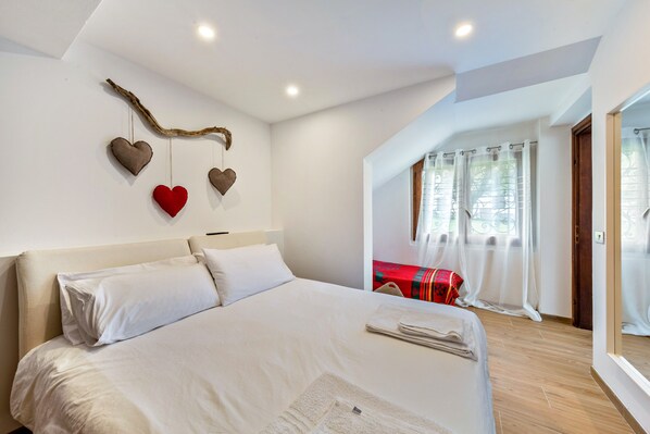 Ein Schlafzimmer mit einem großen Bett, Holzboden, einem fenster mit Vorhängen und einer Wanddekoration.