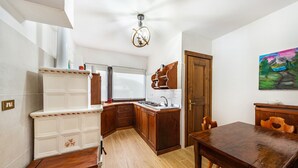 A compact kitchen with wooden cabinets, a white countertop, and a dining area with a wooden table and chairs. - Apartment 'Appartamento Piano Terra 1' with Mountain View, Shared Garden and Wi-Fi (Pieve di Cadore)