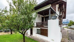 A white building with a balcony, stone steps, and a tree in the foreground. - Apartment 'Appartamento Piano Terra 1' with Mountain View, Shared Garden and Wi-Fi (Pieve di Cadore)