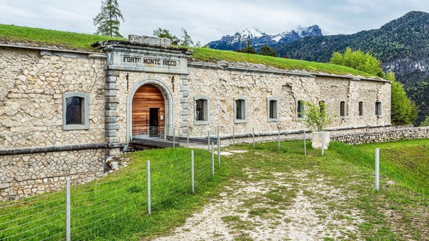 A stone building with a wooden door, labeled 'FORT. MONTE RICCO,' surrounded by a grassy area and mountains in the background. - Apartment 'Appartamento Piano Terra 1' with Mountain View, Shared Garden and Wi-Fi (Pieve di Cadore)
