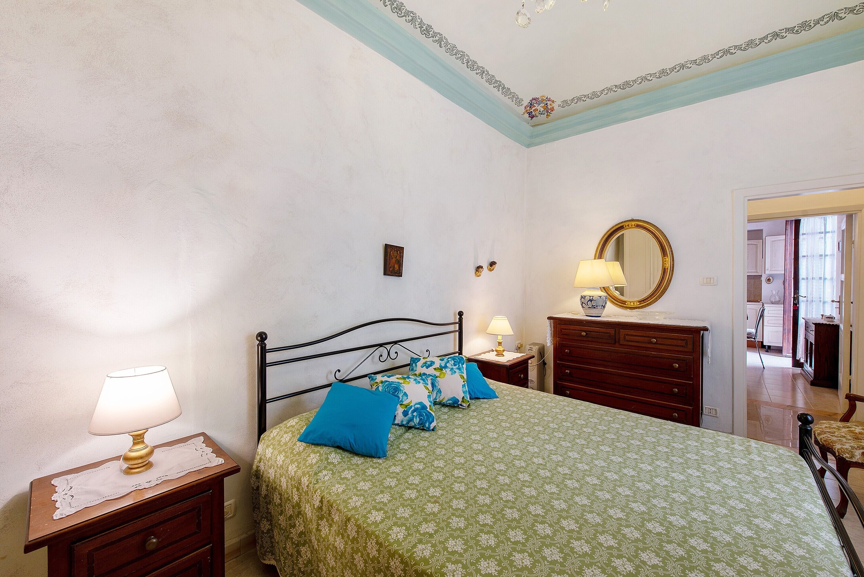 A bedroom with a bed, bedside tables, a dresser, a mirror, and a door leading to another room.