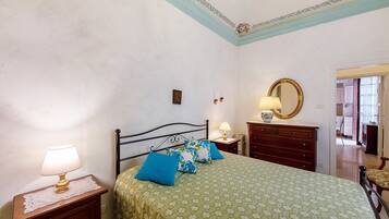 A bedroom with a bed, bedside tables, a dresser, a mirror, and a door leading to another room.