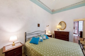 Quarto com cama, mesas de cabeceira, cômoda, espelho e porta para outro espaço.