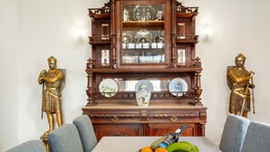 Una mesa de comedor con un frutero, dos estatuas doradas y un aparador con puertas de vidrio.