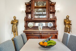 A dining table with a fruit bowl, two golden statues, and a wooden cabinet with glass doors.