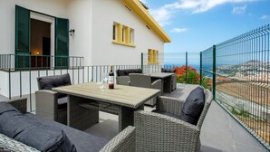 Un patio al aire libre con mobiliario de mimbre, una mesa con una botella y vistas al mar.
