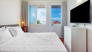 Una habitación de hotel con cama, televisión, cómoda y ventana con cortinas.