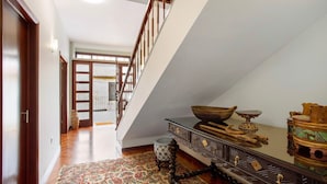 Una escalera que conduce a un segundo piso, piso de madera, alfombra estampada y adornos tradicionales sobre una mesa.