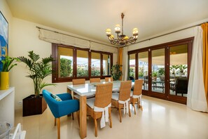 A dining area with a glass table, wicker chairs, a chandelier, and large windows with curtains. - Spacious Villa by the Sea with Private Saltwater Pool (Can Pastilla)