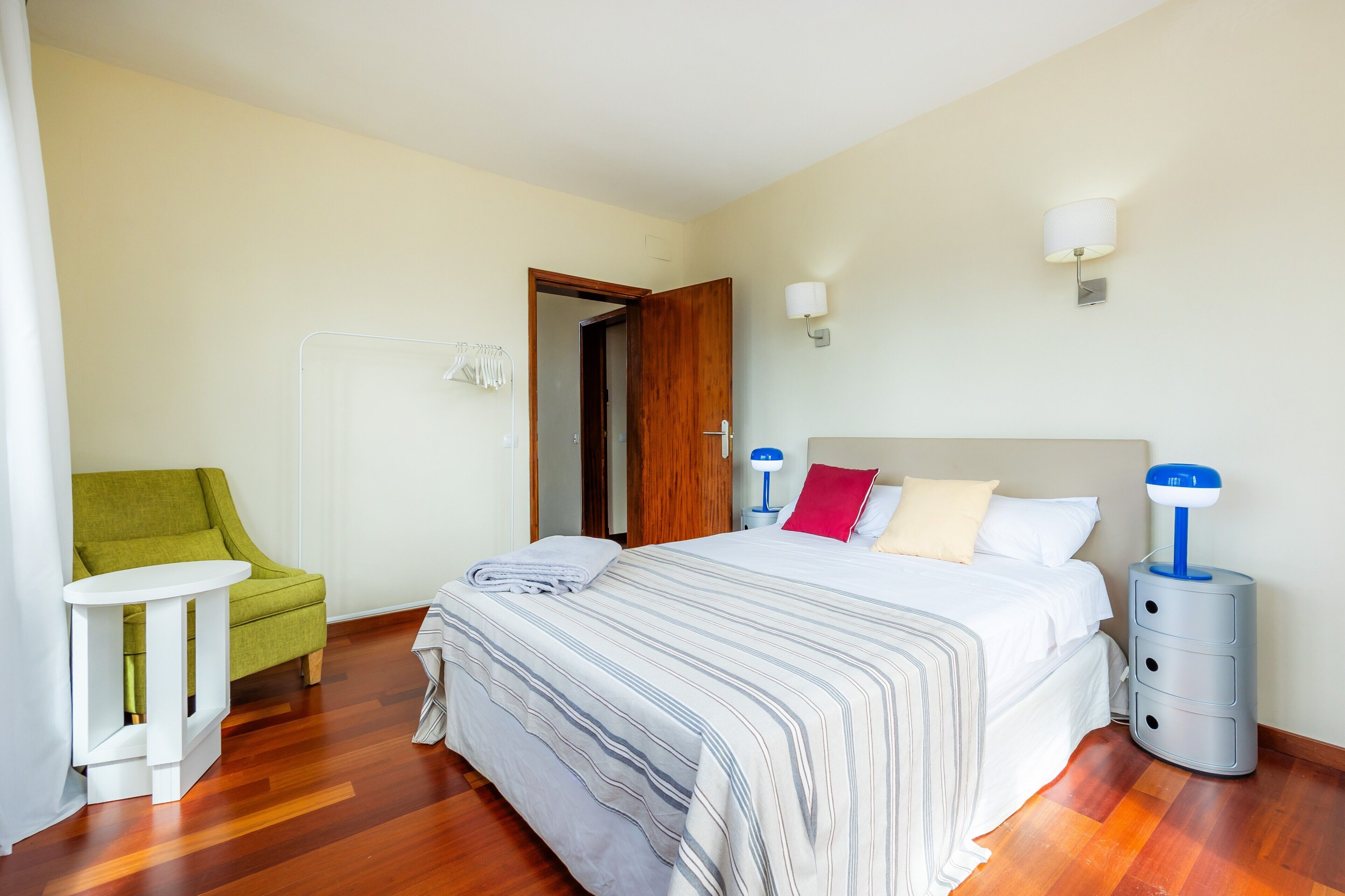 Ein Hotelzimmer mit Bett, Nachttischen, einem Sessel und einer Tür.