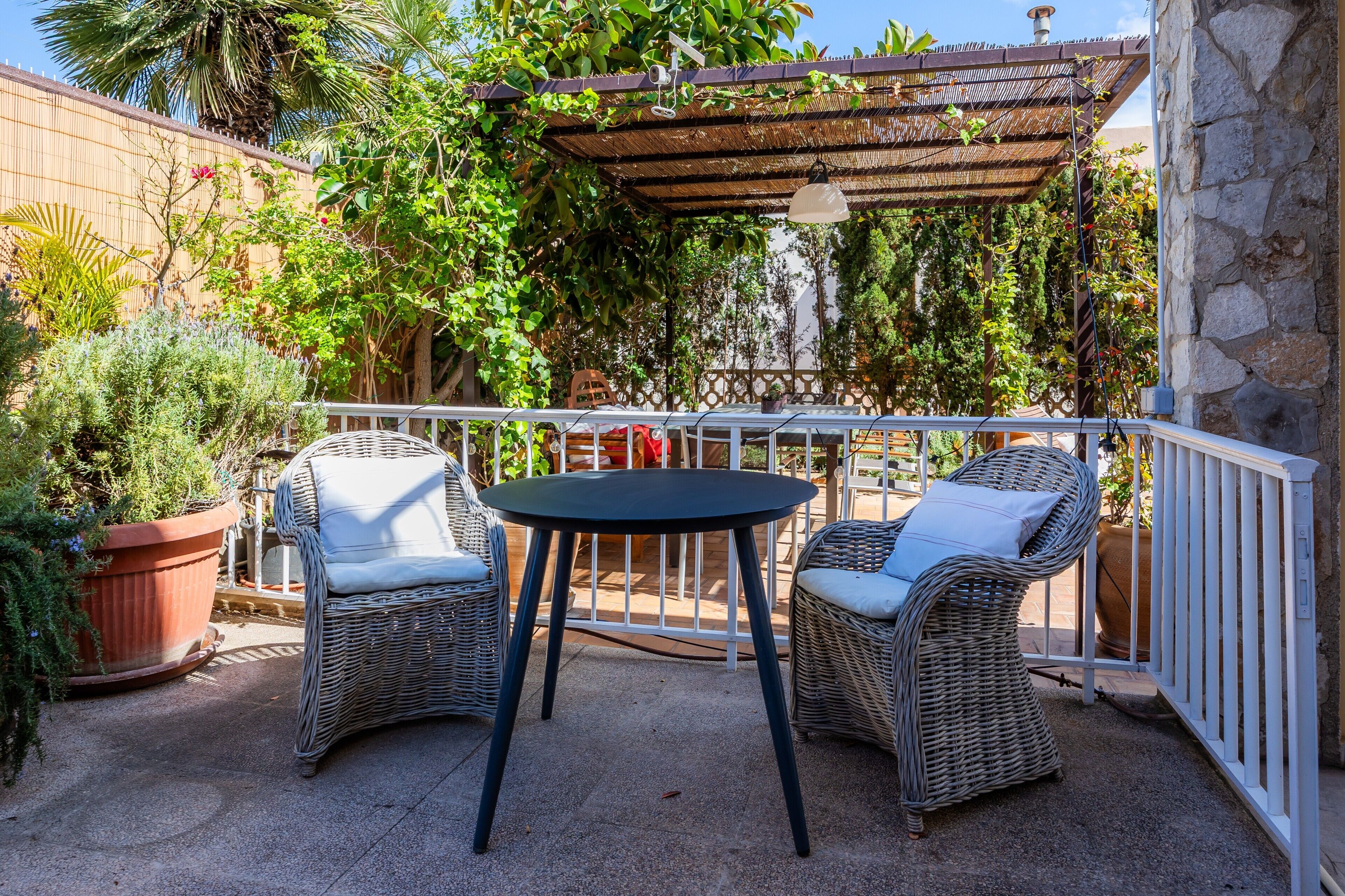 An outdoor patio with wicker furniture, a pergola, and potted plants.