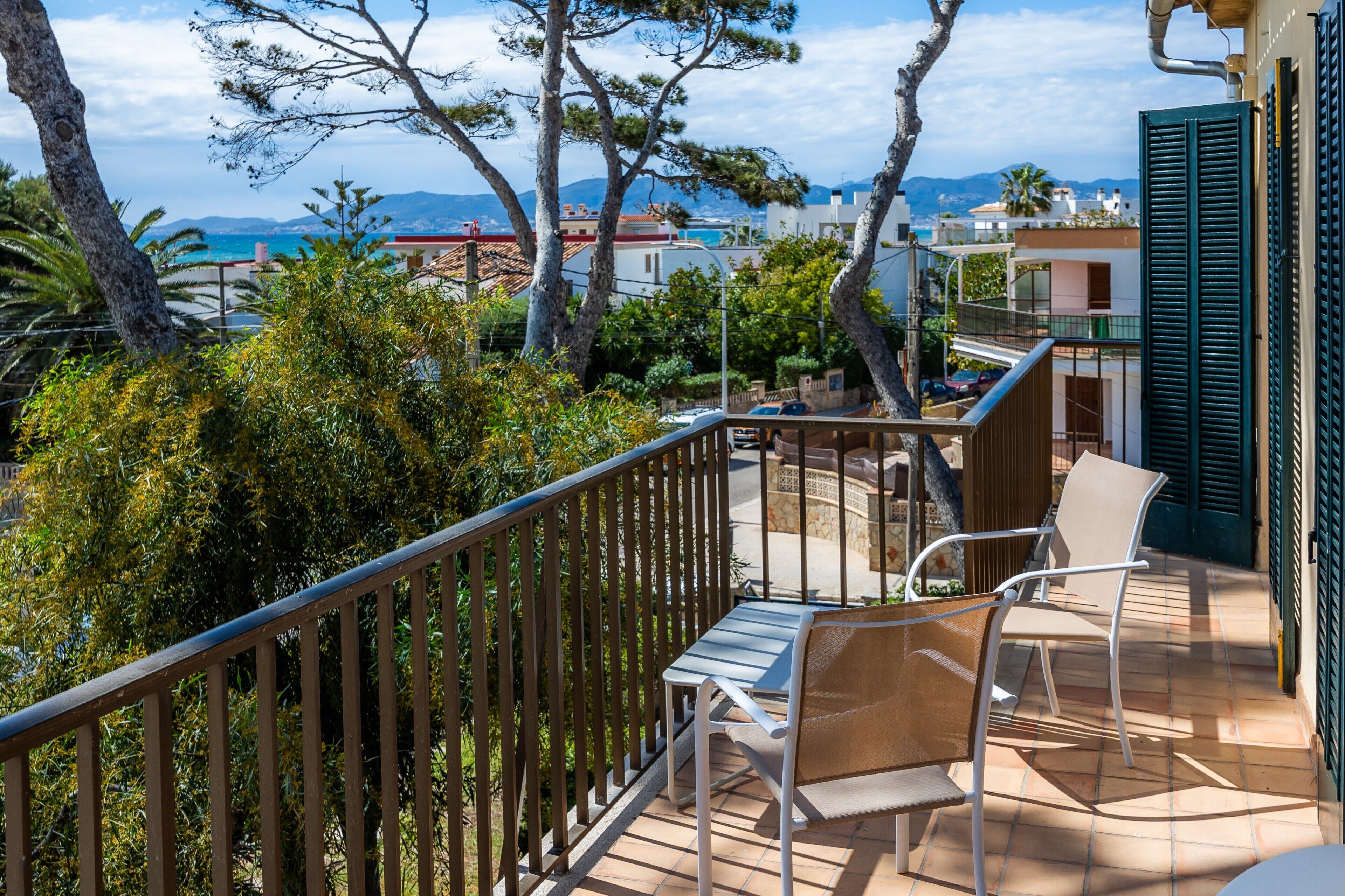 A balcony with a table and chairs, overlooking a coastal area with buildings and trees.