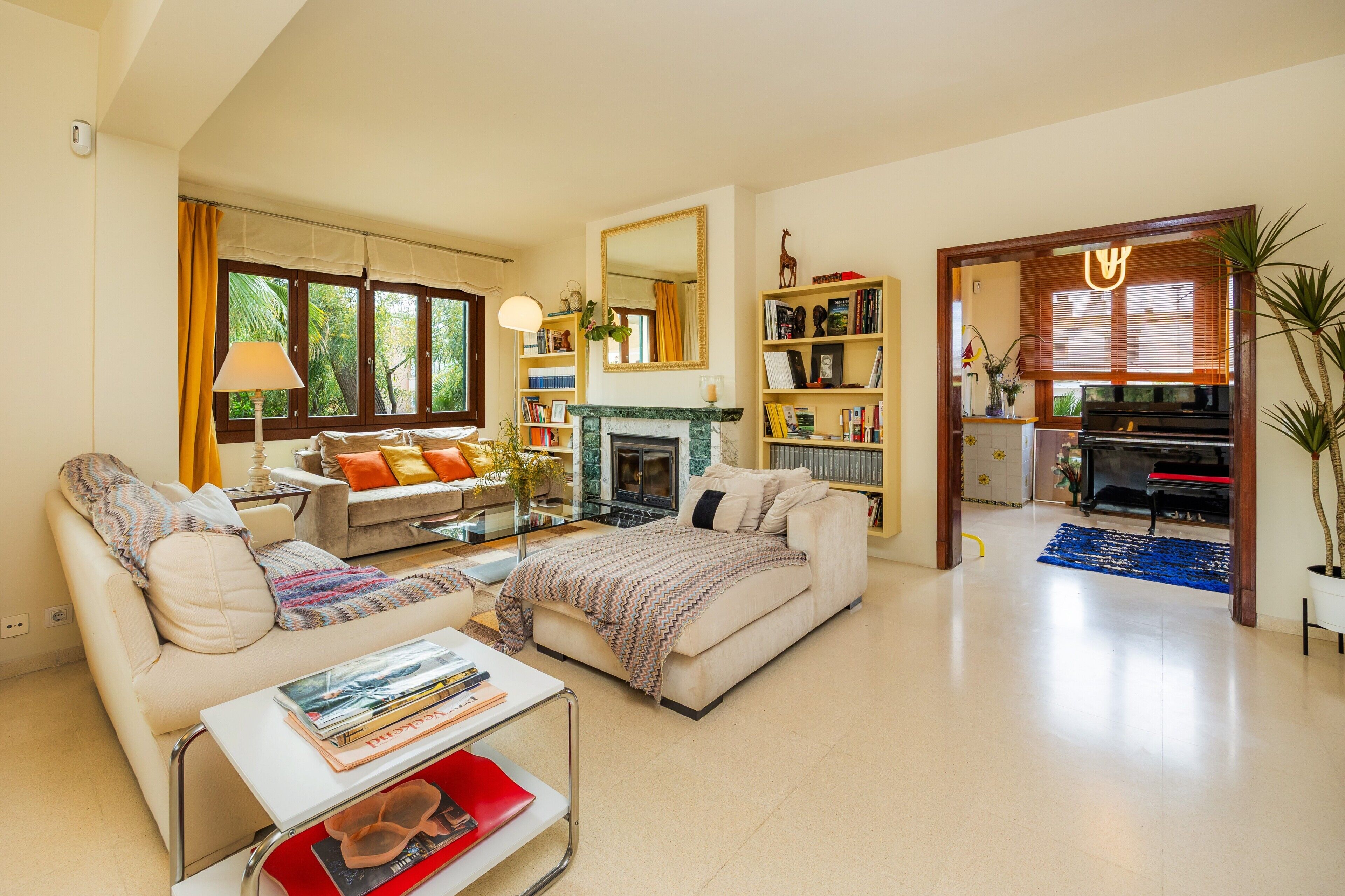 A living room with a sofa, coffee table, fireplace, bookshelf, and a dining area with a piano.