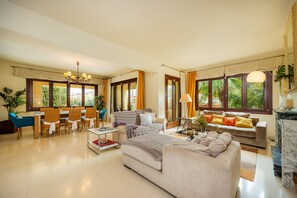 A spacious living area with a dining table, sofas, and a large window with curtains.
