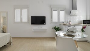 A modern kitchen with a flat-screen TV, white cabinets, and a dining area with a glass table.