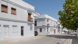 A street with white buildings, a car parked on the side, and a clear blue sky.