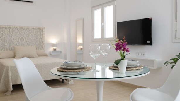 A modern hotel room with a bed, a round glass table with two chairs, a TV, and a window.