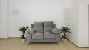 A grey sofa in a room with light wooden flooring, white walls, and two potted plants.