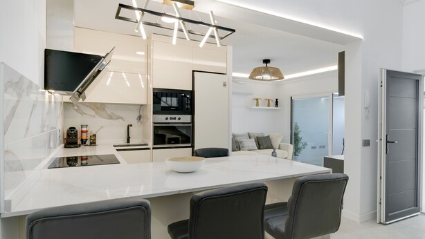 Una cocina moderna con una isla central, electrodomésticos integrados y una zona de comedor con sillas.