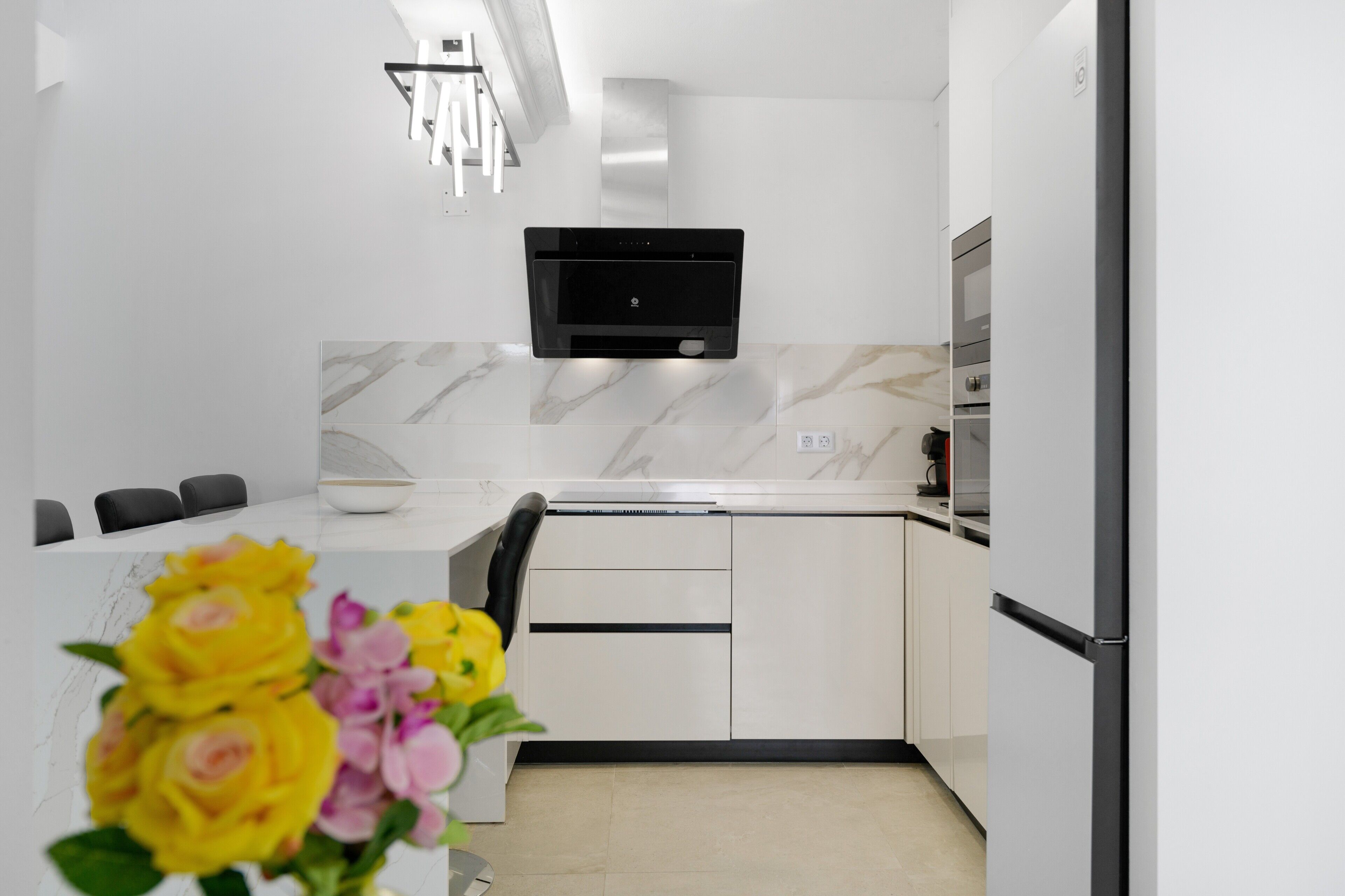 A modern kitchen with white cabinetry, a built-in microwave, and a marble backsplash.