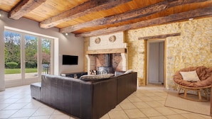 A living room with a fireplace, a sofa, a television, and a stone wall. - Stone House with Private Pool and Garden – Charm & Comfort in Dordogne (La Chapelle-Gonaguet)