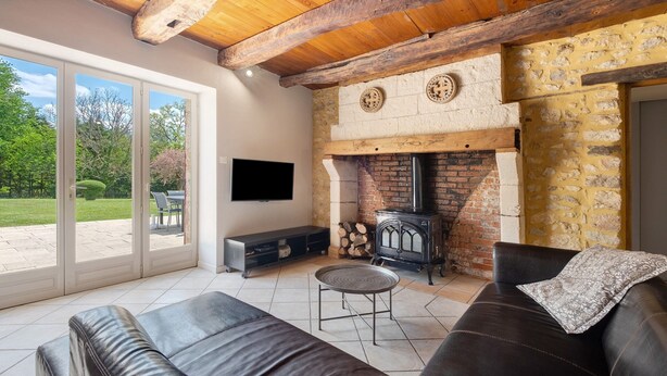 A living room with a fireplace, leather sofas, a television, and a stone wall. - Stone House with Private Pool and Garden – Charm & Comfort in Dordogne (La Chapelle-Gonaguet)