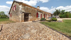 A stone building with a wooden door, red shutters, and a gravel pathway leading to the entrance. - Stone House with Private Pool and Garden – Charm & Comfort in Dordogne (La Chapelle-Gonaguet)